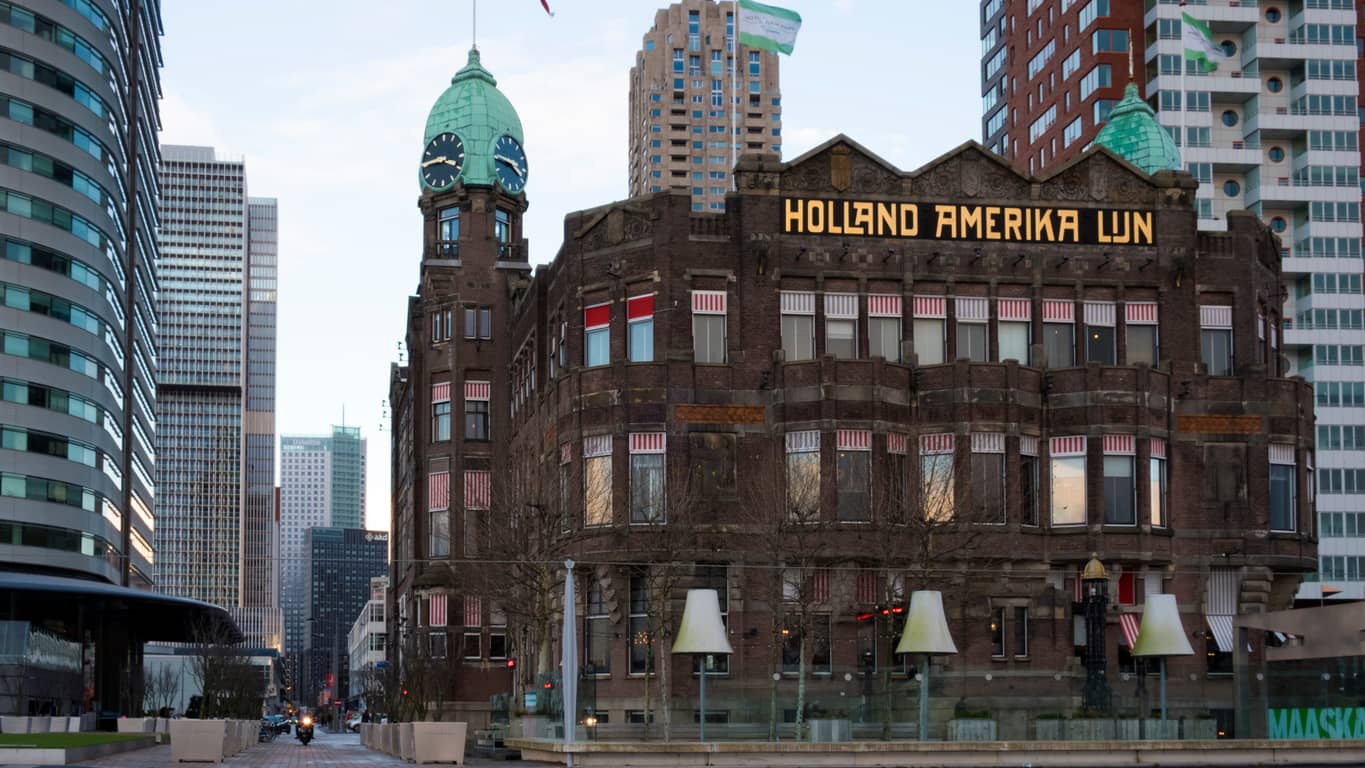 Historic red-brick Holland Amerika Lijn building with the sign on the facade, set among modern skyscrapers on a city street.