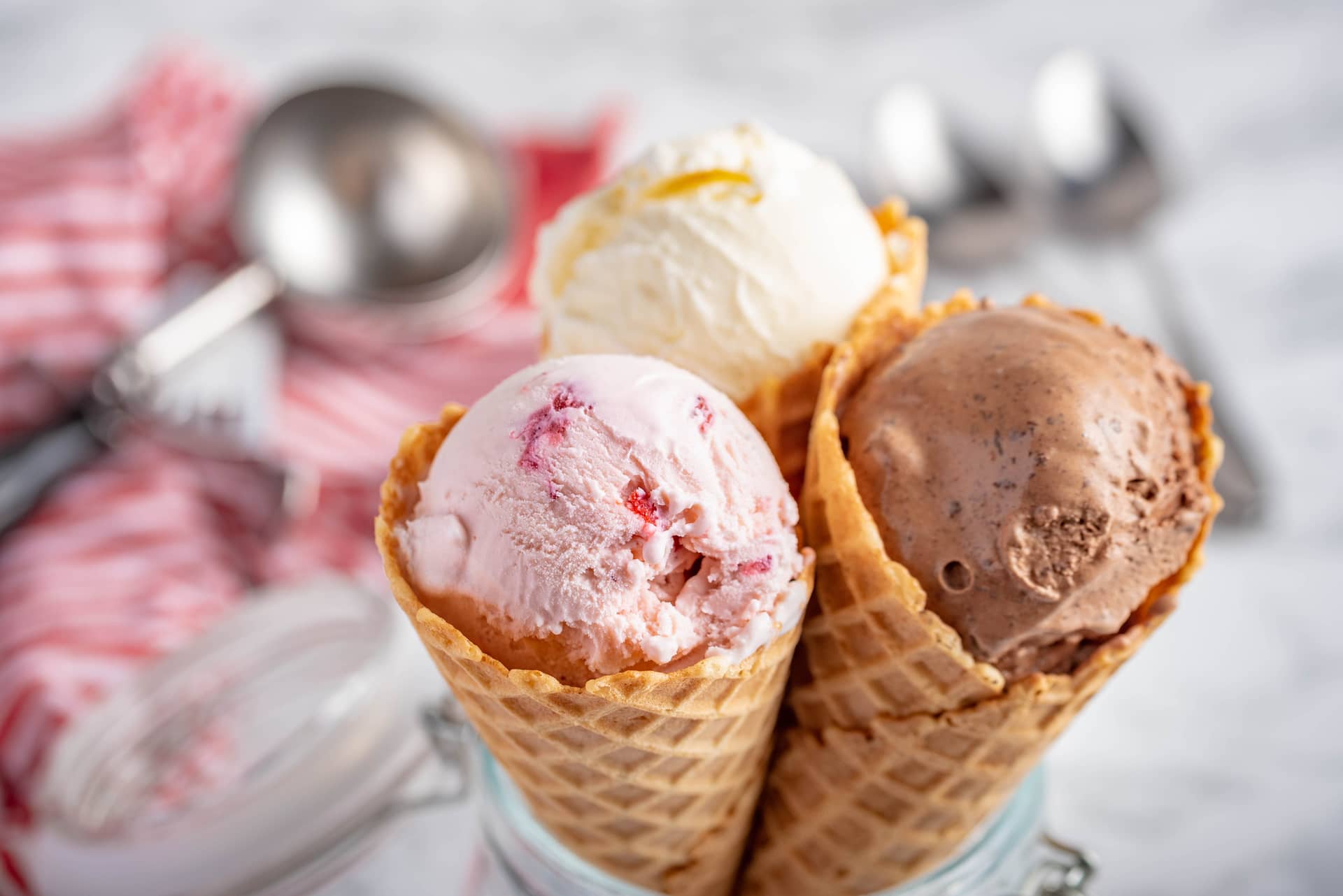 Three waffle cones filled with scoops of pink strawberry, vanilla, and chocolate ice cream stacked together in a glass jar.