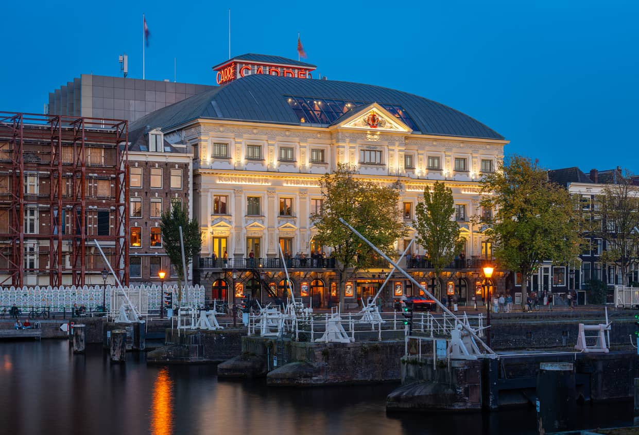 Historic neoclassical building along a canal at dusk, illuminated windows and decorative facade reflecting in calm water