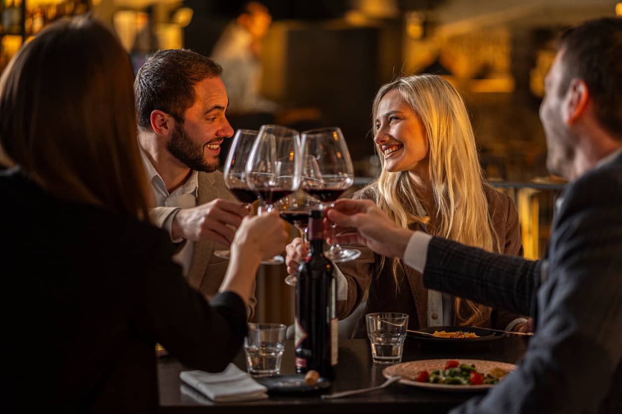 Group of four friends toasting with red wine at a warmly lit restaurant.