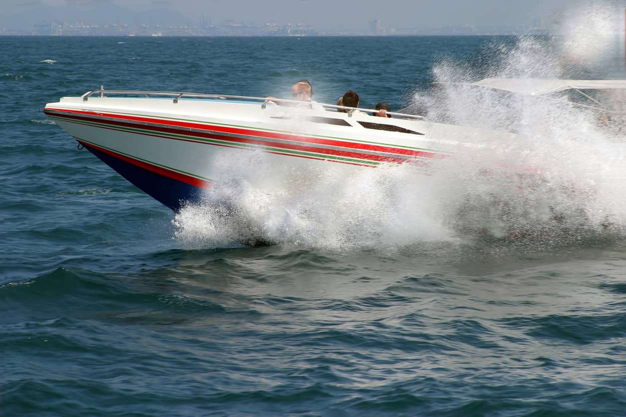 Speedboat speeding across the water, creating a large spray as it cuts through waves with passengers onboard.