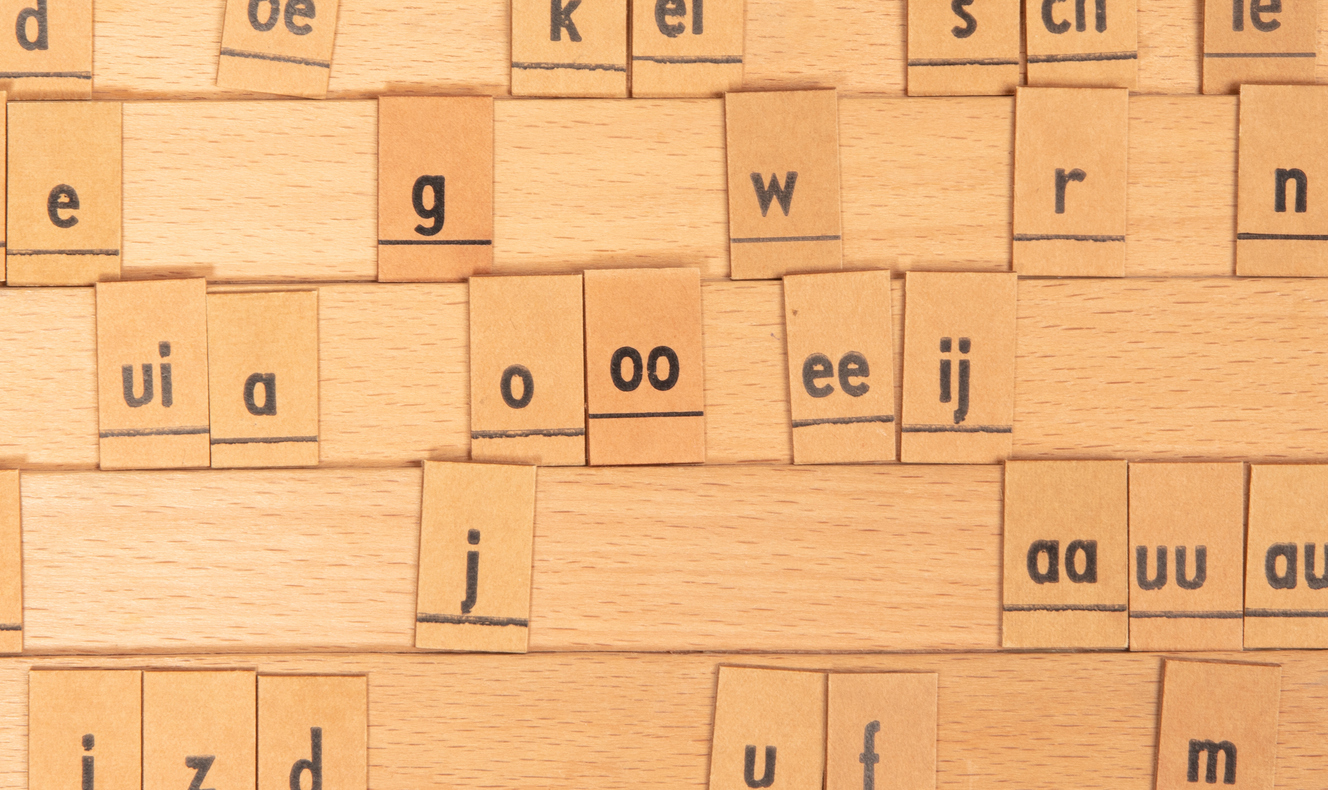 Close-up of wooden letter tiles scattered on a light wood table surface.